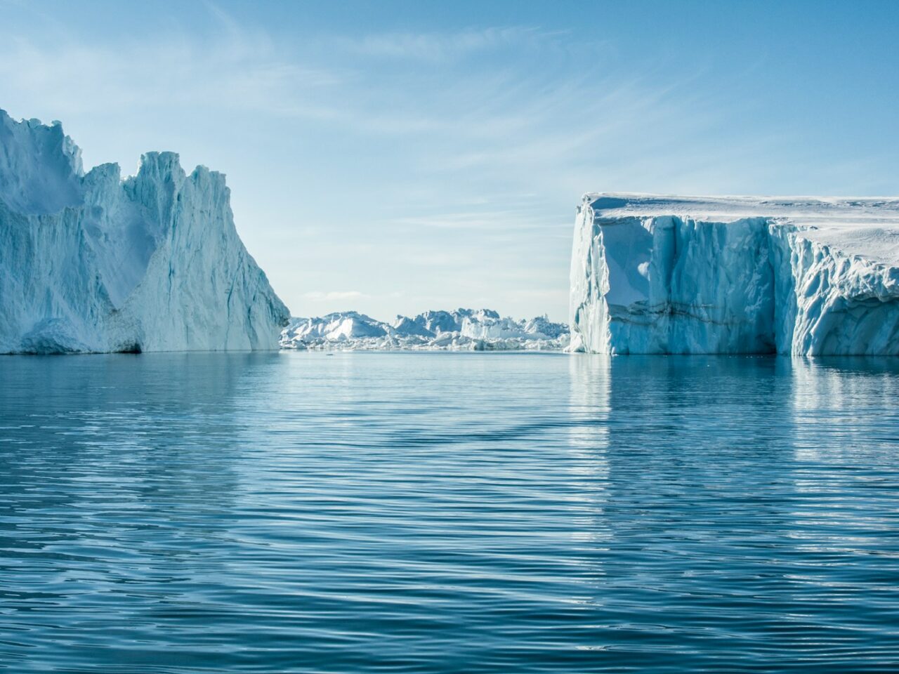 icebergs on body of water under blue and white sky at daytime